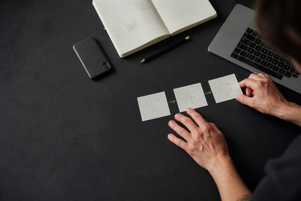 A builder arranging three idea cards beside a notebook and laptop